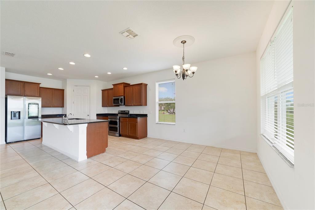 A kitchen with wood cabinets, a center island, and tile flooring opens to a dining area — 3880 CARRICK BEND DRIVE, KISSIMMEE, FL