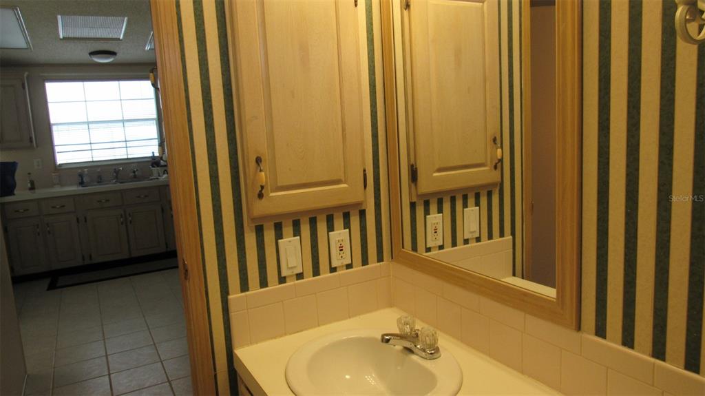 A bathroom vanity with a sink and mirror sits in front of striped wallpaper — 2103 STACEY DRIVE, MOUNT DORA, FL