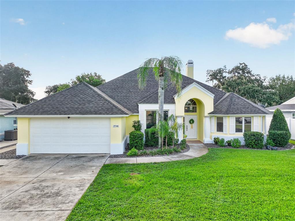 A yellow single-story house with a two-car garage, a palm tree, and a green lawn — 35546 CEDAR LANE, LEESBURG, FL