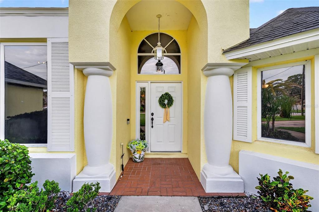 A yellow house entrance features a white door, two large columns, and a brick porch — 35546 CEDAR LANE, LEESBURG, FL