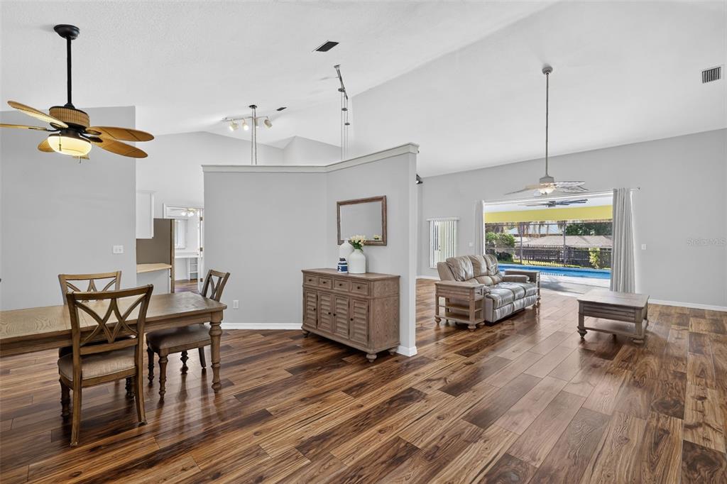 An open-concept living and dining area features wood-look flooring, a partial wall, and a pool view — 35546 CEDAR LANE, LEESBURG, FL