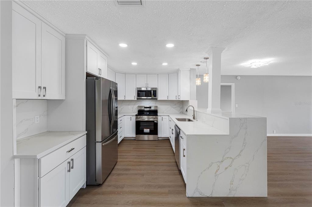 A modern kitchen features white cabinets, stainless steel appliances, and white marble-patterned countertops — 100 BLUFF VIEW DRIVE UNIT 404C, BELLEAIR BLUFFS, FL