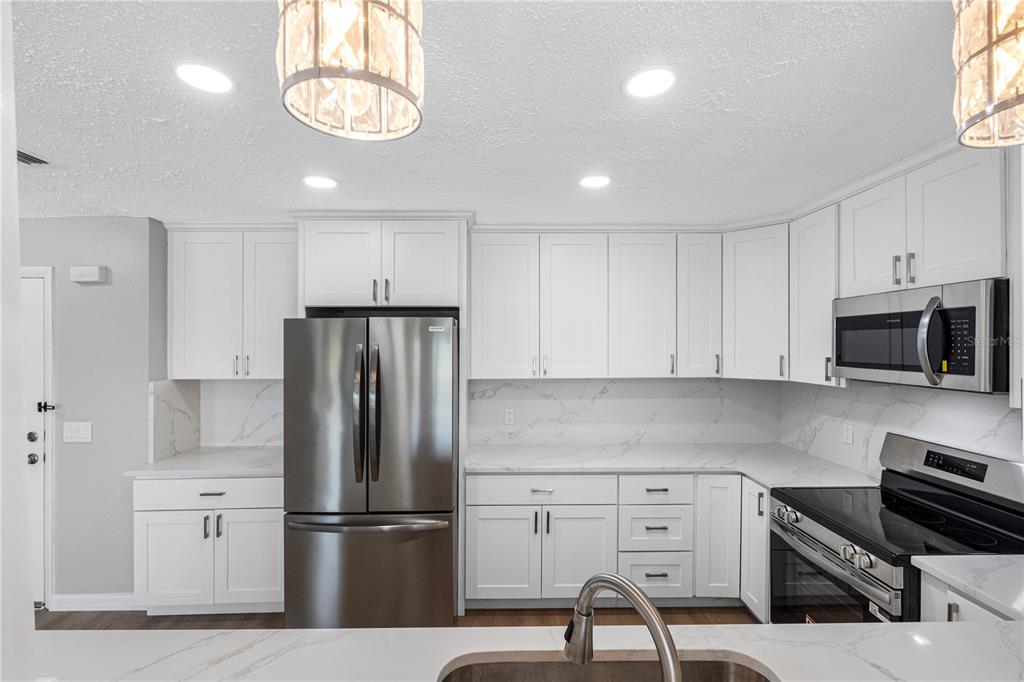 A modern kitchen features white cabinets, stainless steel appliances, and white quartz countertops — 100 BLUFF VIEW DRIVE UNIT 404C, BELLEAIR BLUFFS, FL