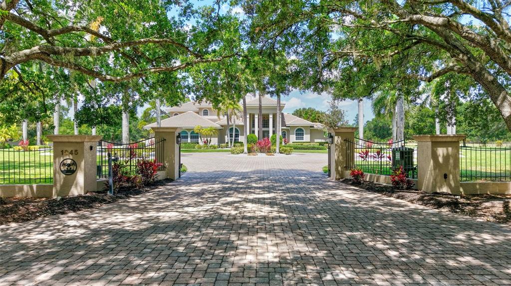 A paved driveway leads through a gated entrance toward a large two-story house — 1045 FOX CREEK DRIVE, SARASOTA, FL