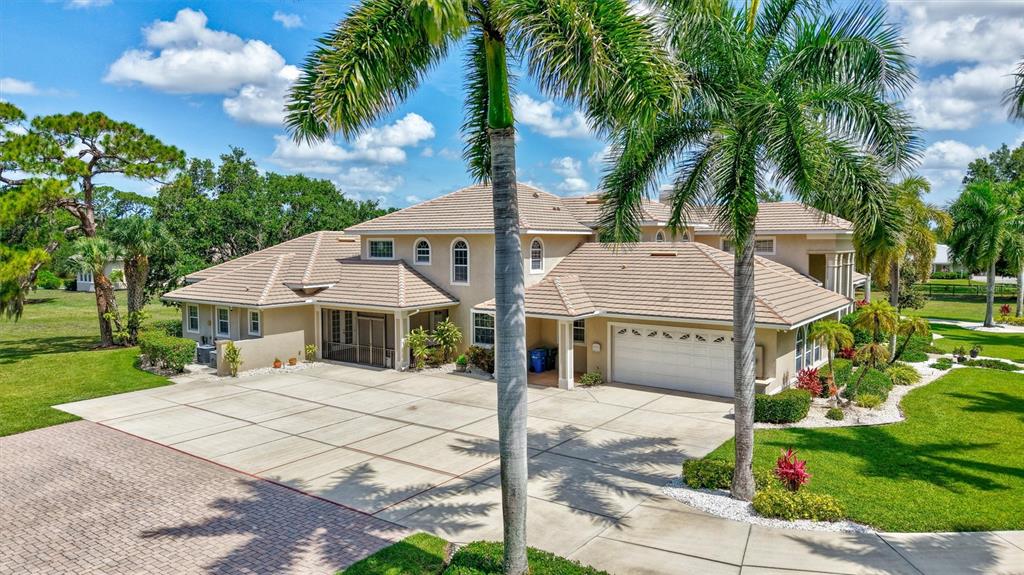 A large tan house with a tiled roof features a spacious concrete driveway and palm trees — 1045 FOX CREEK DRIVE, SARASOTA, FL