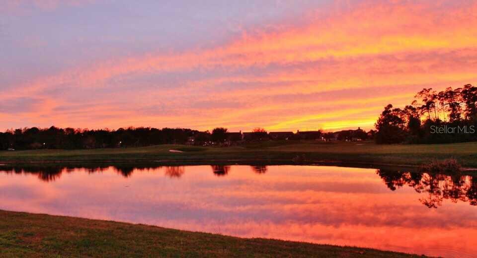 A vibrant sunset reflects over a calm pond in front of a golf course landscape — 934 WESTPARK DRIVE, CELEBRATION, FL