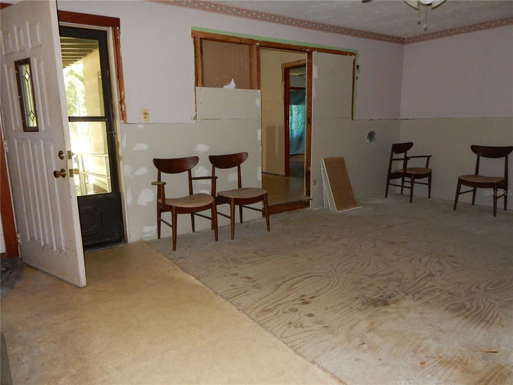 An unfinished room features exposed plywood flooring, partially drywalled walls, and four wooden chairs — 38036 CENTRAL AVENUE, ZEPHYRHILLS, FL