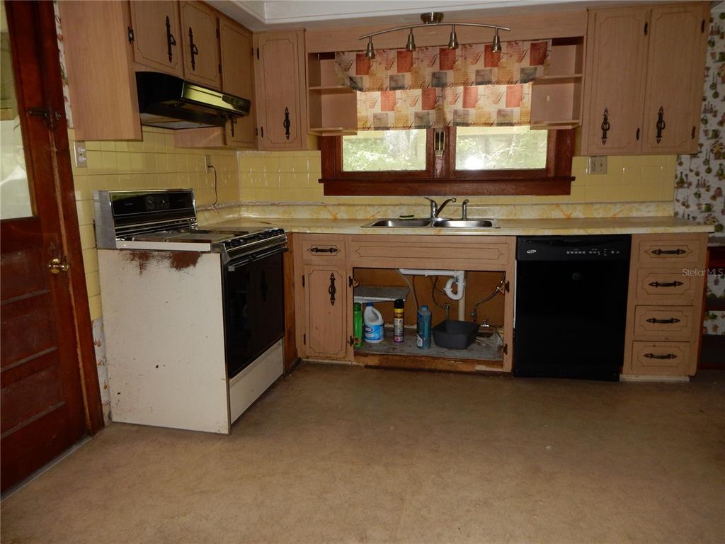 A kitchen features light wood cabinets, yellow tile backsplash, a white stove, and an open sink — 38036 CENTRAL AVENUE, ZEPHYRHILLS, FL