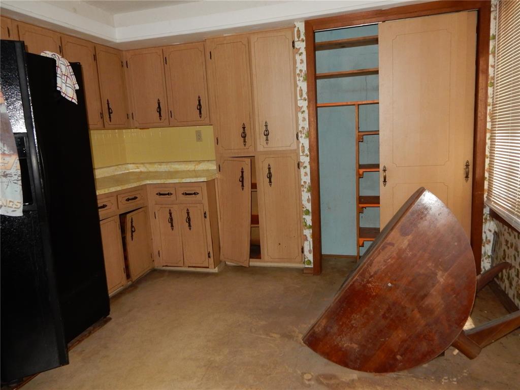 A kitchen features light wood cabinets, a black refrigerator, and a table tipped on its side — 38036 CENTRAL AVENUE, ZEPHYRHILLS, FL