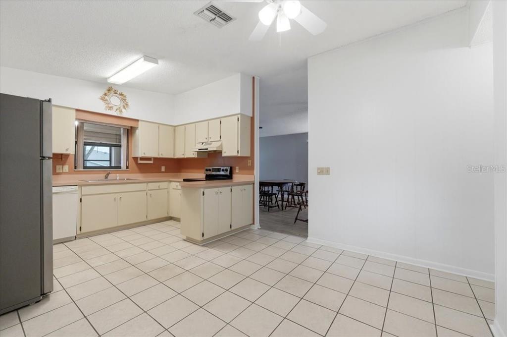 A kitchen with white tile floors, light-colored cabinets, a stainless steel refrigerator, and a ceiling fan — 3231 BEAR CREEK LANE, LAKELAND, FL