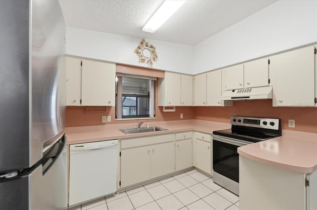 A kitchen features white cabinets, pink countertops, a stainless steel refrigerator, and tiled flooring — 3231 BEAR CREEK LANE, LAKELAND, FL