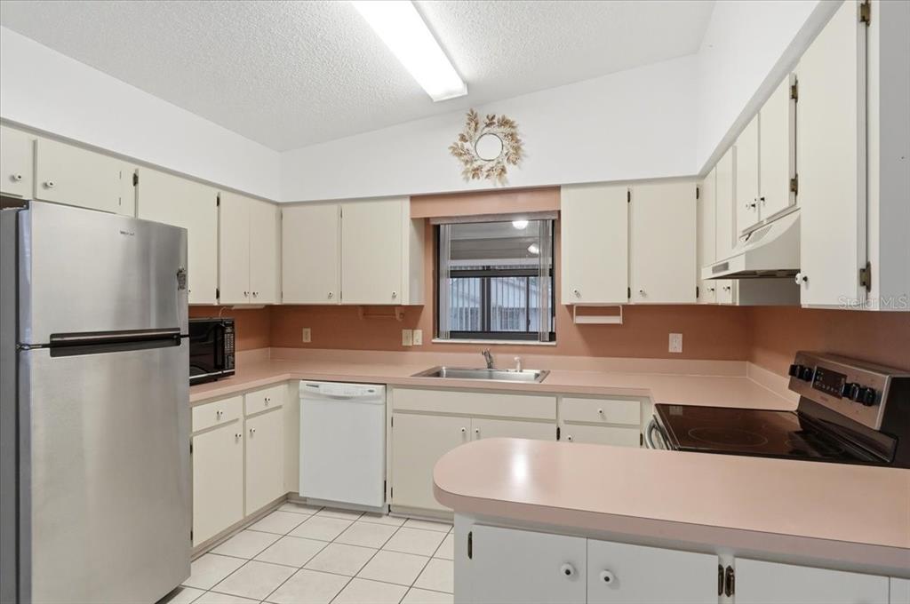 A kitchen features white cabinets, pink countertops, a stainless steel refrigerator, and tiled flooring — 3231 BEAR CREEK LANE, LAKELAND, FL