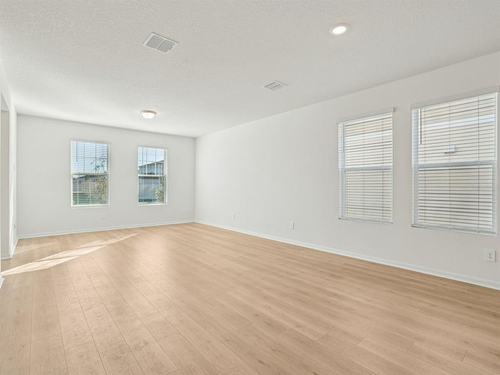 An empty room with light wood-look flooring, white walls, and several windows with blinds — 4685 CROSS PRAIRIE PARKWAY, ST CLOUD, FL