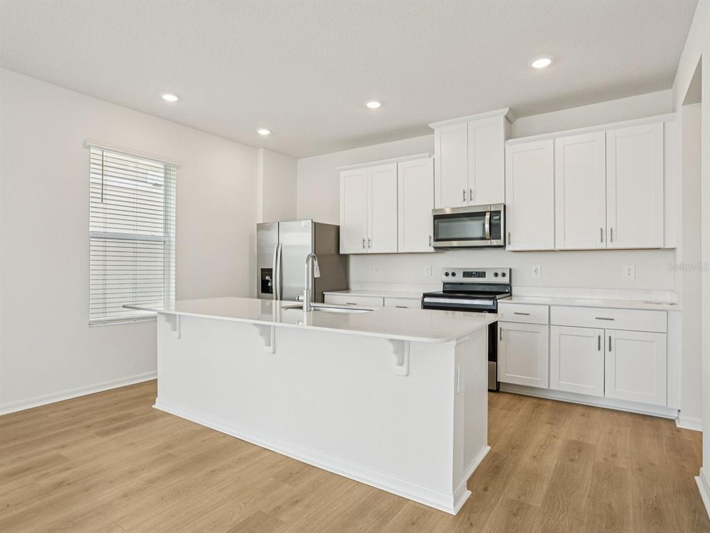 A modern kitchen features white cabinets, stainless steel appliances, and a large central island — 4685 CROSS PRAIRIE PARKWAY, ST CLOUD, FL