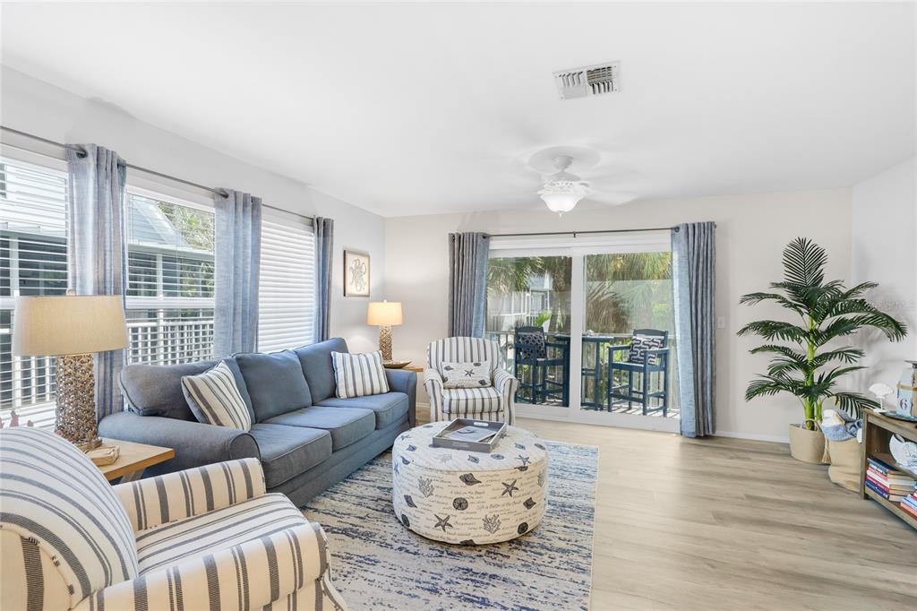 A living room features a blue sofa, striped armchairs, a patterned ottoman, and sliding glass doors — 6250 HOLMES BOULEVARD UNIT 24, HOLMES BEACH, FL