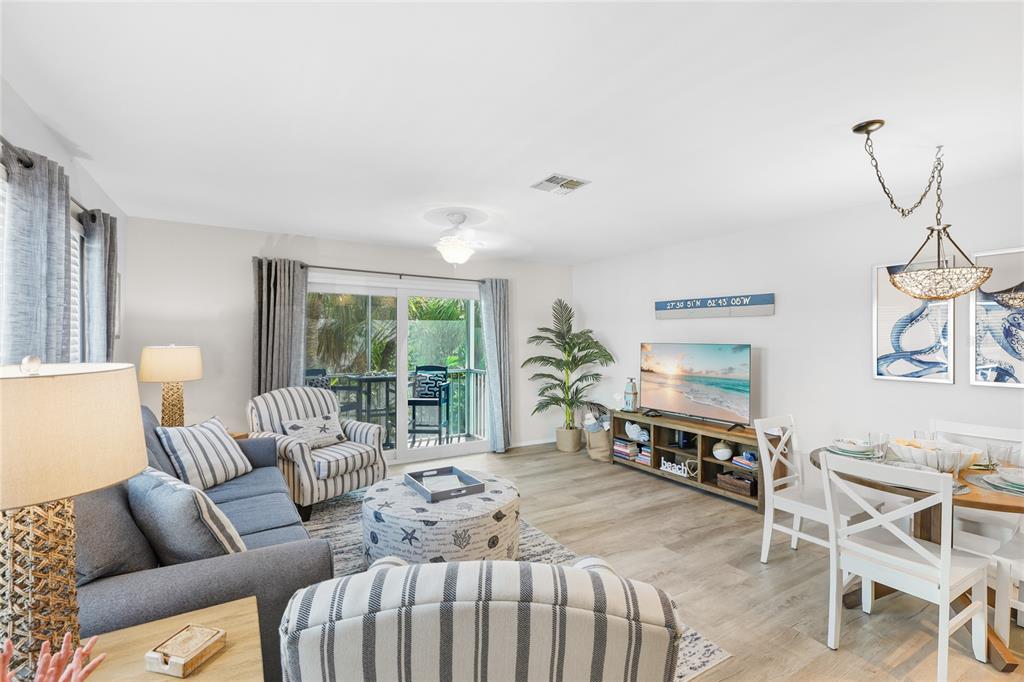 A living room and dining area feature light wood floors, coastal decor, and a sliding door — 6250 HOLMES BOULEVARD UNIT 24, HOLMES BEACH, FL
