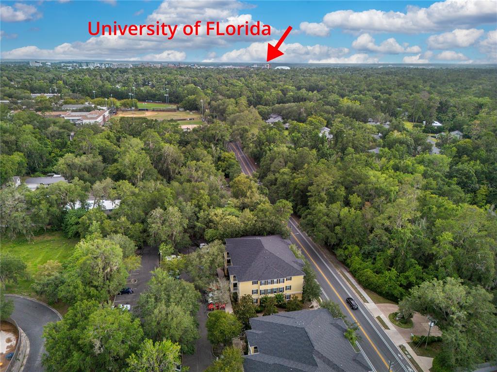 An aerial view shows a multi-story apartment building surrounded by trees near a road — 2227 NW 16TH TERRACE, GAINESVILLE, FL