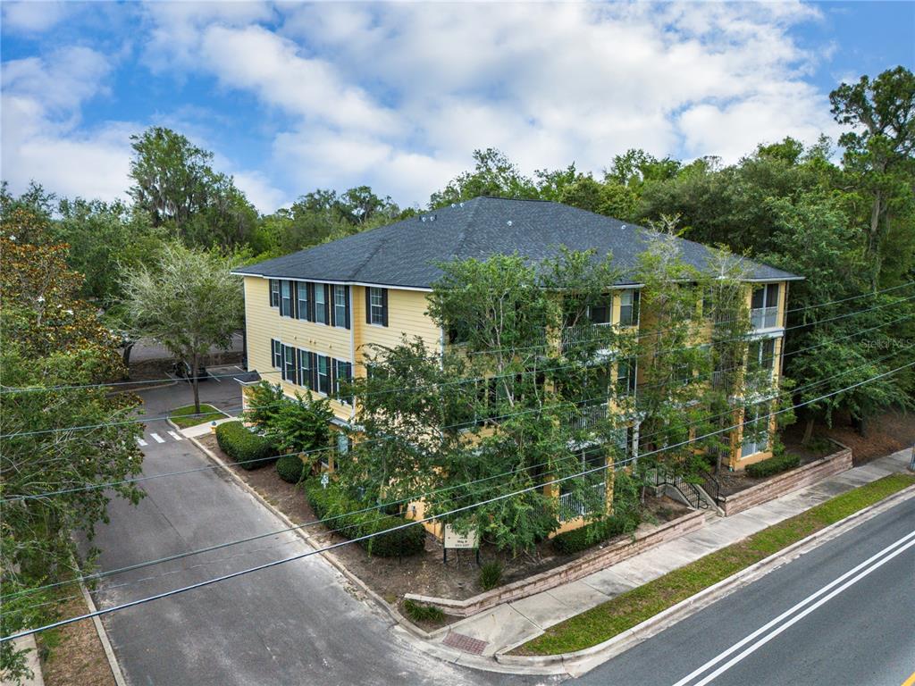 An exterior view of a three-story yellow apartment building with a dark shingled roof — 2227 NW 16TH TERRACE, GAINESVILLE, FL