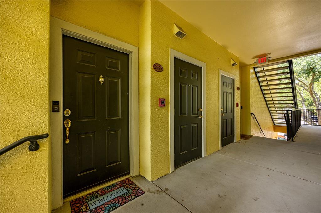 An exterior view of a yellow apartment building hallway with three dark doors and stairs — 2227 NW 16TH TERRACE, GAINESVILLE, FL