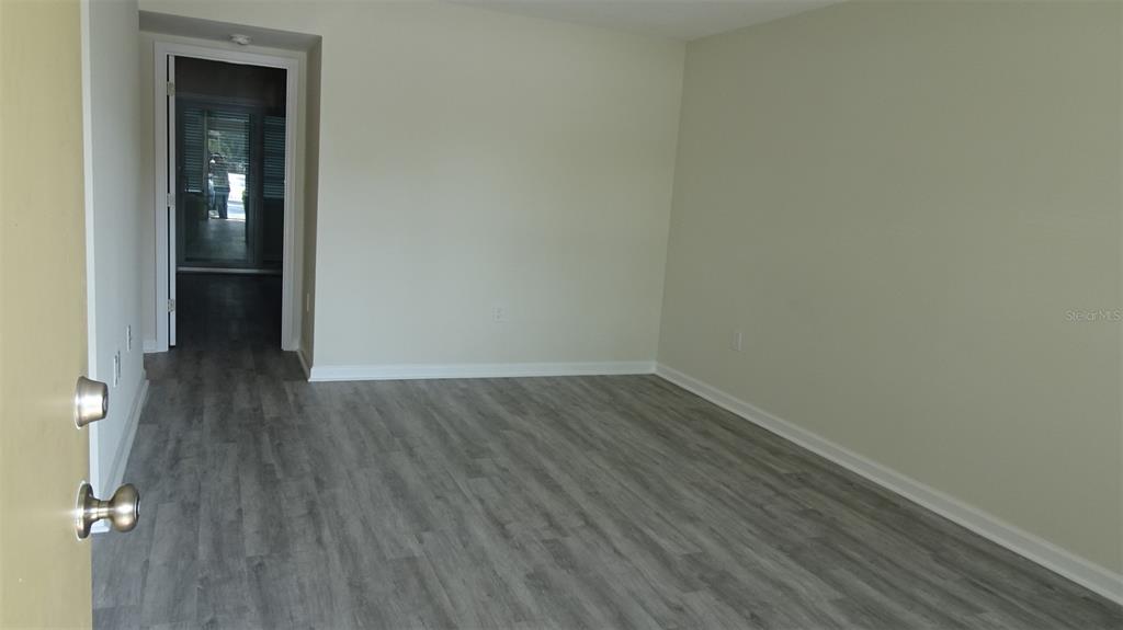 An empty room with light-colored walls and gray wood-look flooring leads to a doorway — 8100 DR MARTIN LUTHER KING JR STREET N UNIT 105, ST PETERSBURG, FL