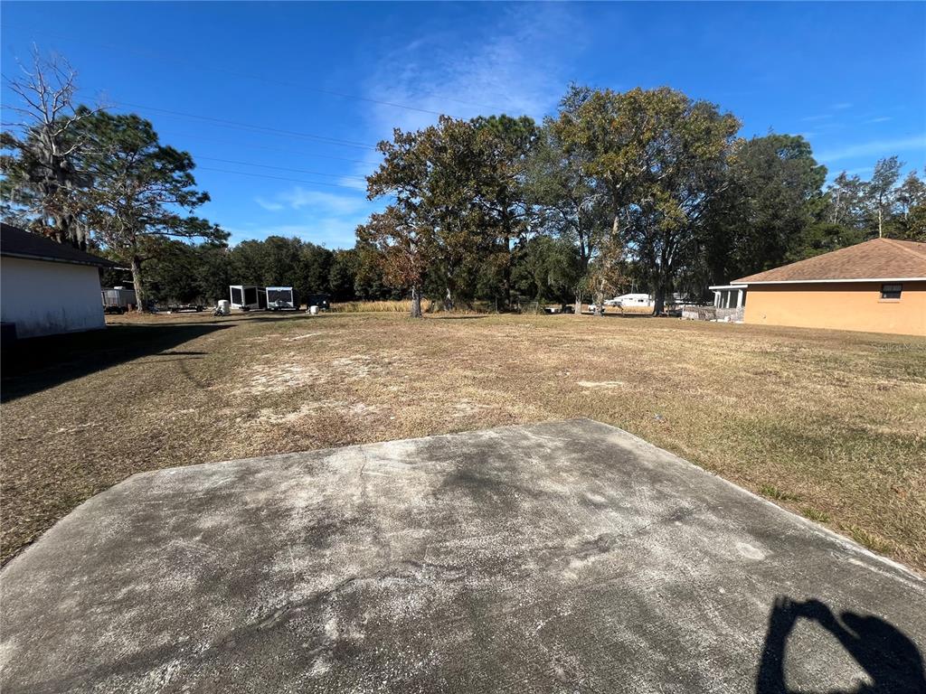 A large, grassy backyard sits between two houses with a concrete pad in the foreground — 26 PINE RUN, OCALA, FL