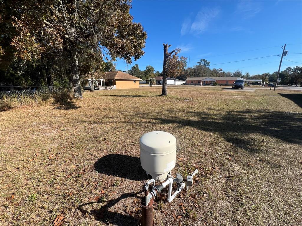 A well pump and pressure tank sit in a grassy yard with nearby houses — 26 PINE RUN, OCALA, FL