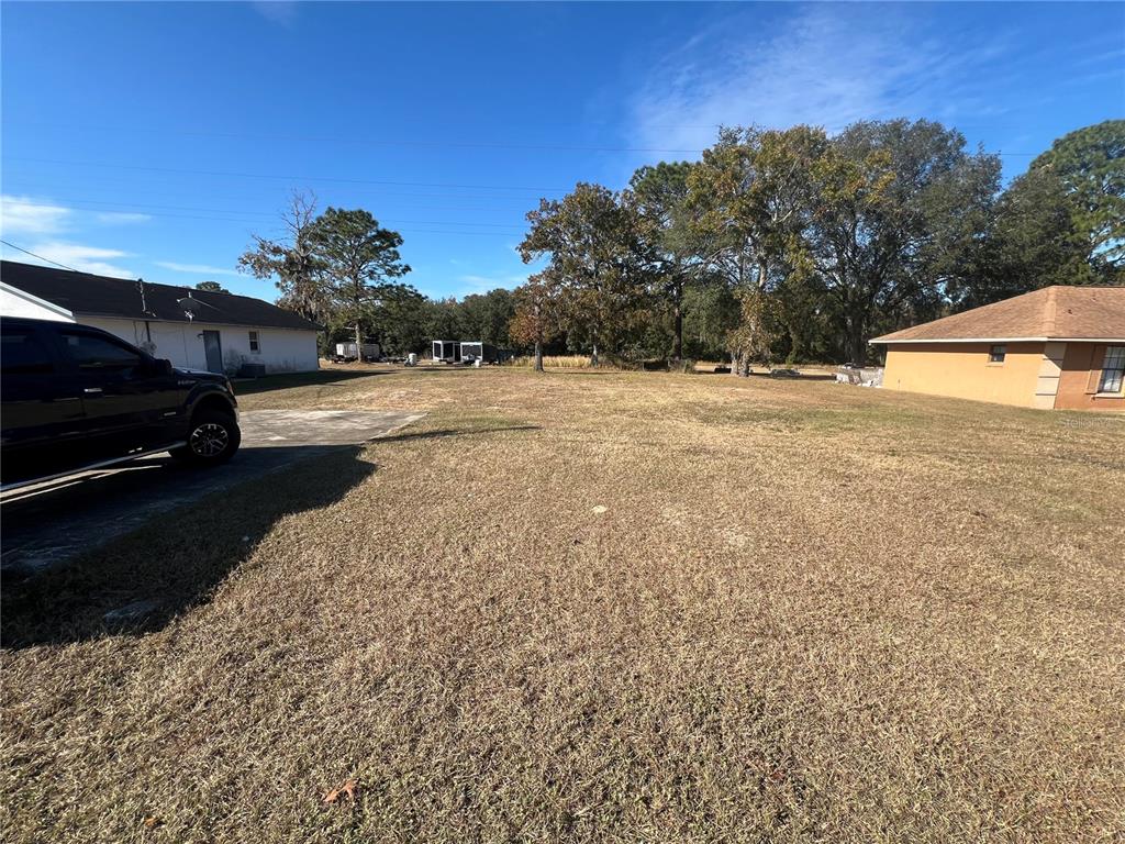 A large, grassy vacant lot sits between two residential houses under a clear blue sky — 26 PINE RUN, OCALA, FL