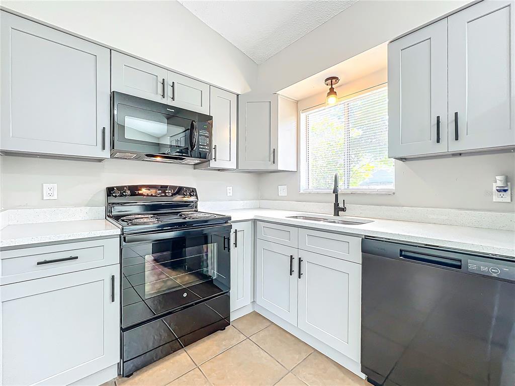 A kitchen features light gray cabinets, black appliances, white countertops, and tile flooring — 13868 LENA STREET, ORLANDO, FL