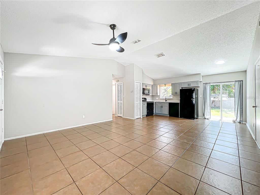 An open-concept living room and kitchen featuring tile flooring, vaulted ceilings, and a ceiling fan — 13868 LENA STREET, ORLANDO, FL