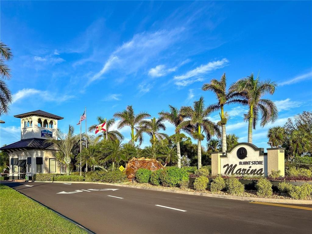 A paved road leads to the entrance of Burnt Store Marina with palm trees and signage — 2064 LITTLE PINE CIRCLE, PUNTA GORDA, FL