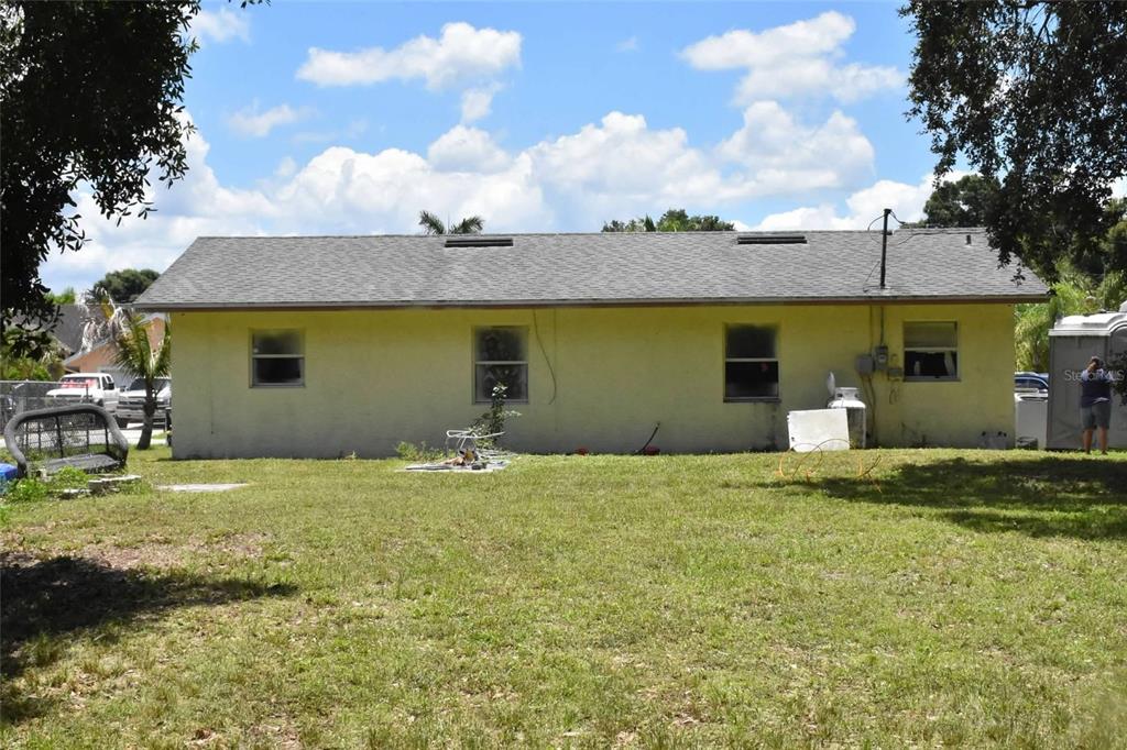 The exterior of a single-story, yellow-stucco house with a gray shingled roof and yard — 907 PINE STREET, IMMOKALEE, FL