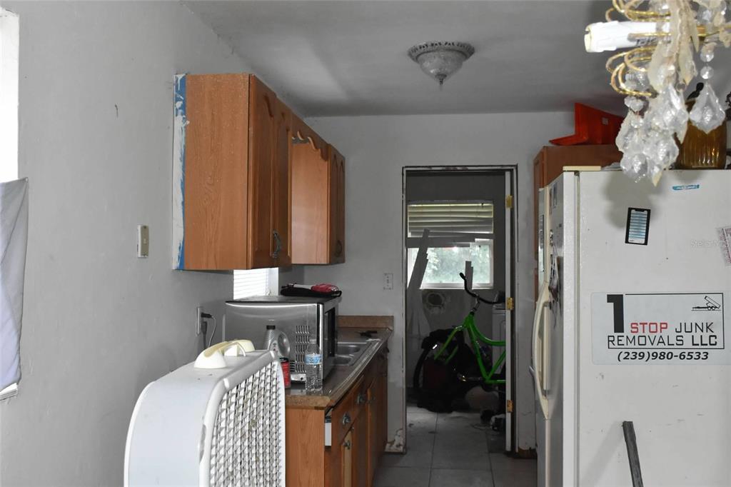 A kitchen features wooden cabinets, a microwave, a refrigerator, and a doorway leading outside — 907 PINE STREET, IMMOKALEE, FL