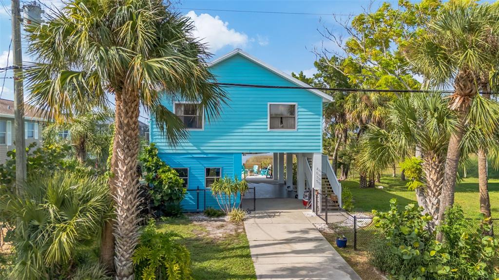 A two-story, light blue stilt house with a concrete driveway and surrounding palm trees — 4035 EAGLE NEST DRIVE, HERNANDO BEACH, FL