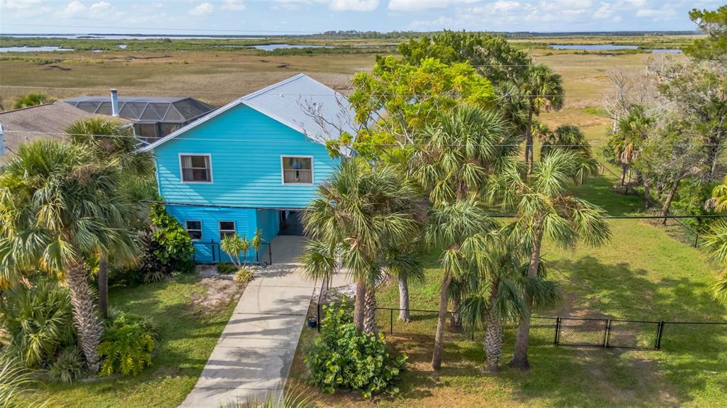 An elevated bright blue house with a metal roof sits on a grassy lot — 4035 EAGLE NEST DRIVE, HERNANDO BEACH, FL