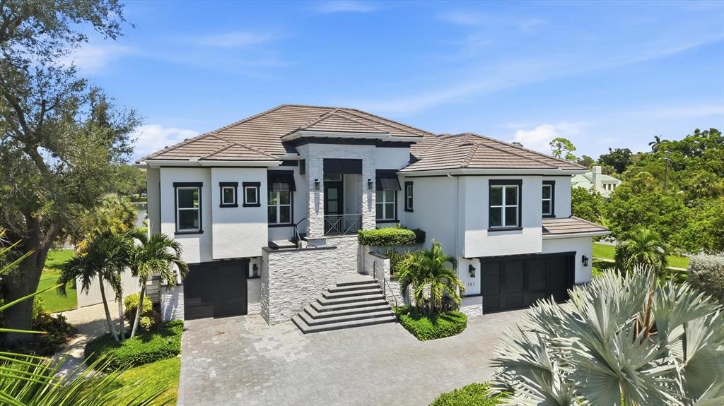 A two-story house with white stucco walls, stone accents, a tiled roof, and a driveway — 387 S SHORE DRIVE, SARASOTA, FL