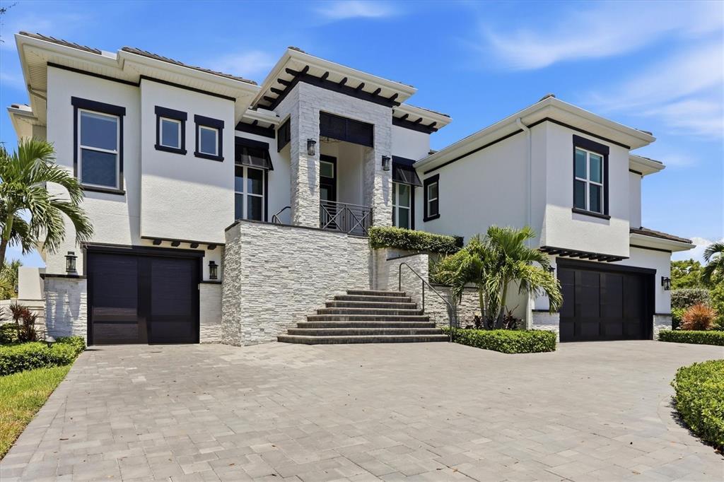 A two-story house with white stucco walls, dark trim, stone accents, and a paved driveway — 387 S SHORE DRIVE, SARASOTA, FL