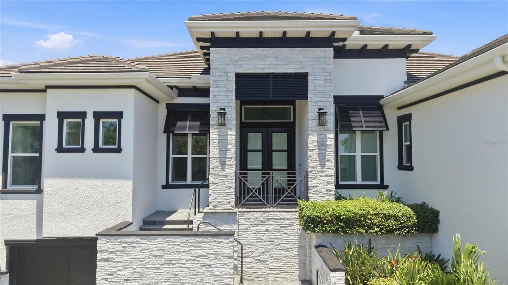 A modern house exterior features white stucco walls, black trim, and a stone-clad entryway — 387 S SHORE DRIVE, SARASOTA, FL