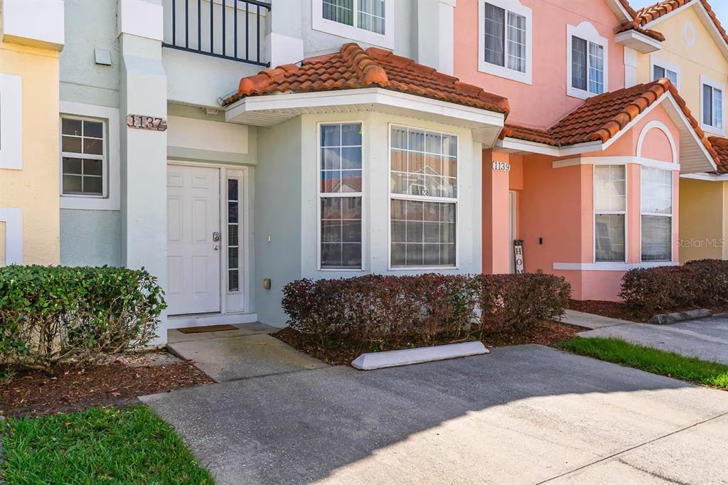 The exterior of two adjacent townhomes features light-colored stucco, tile roofs, and concrete driveways — 1137 S BEACH CIRCLE, KISSIMMEE, FL