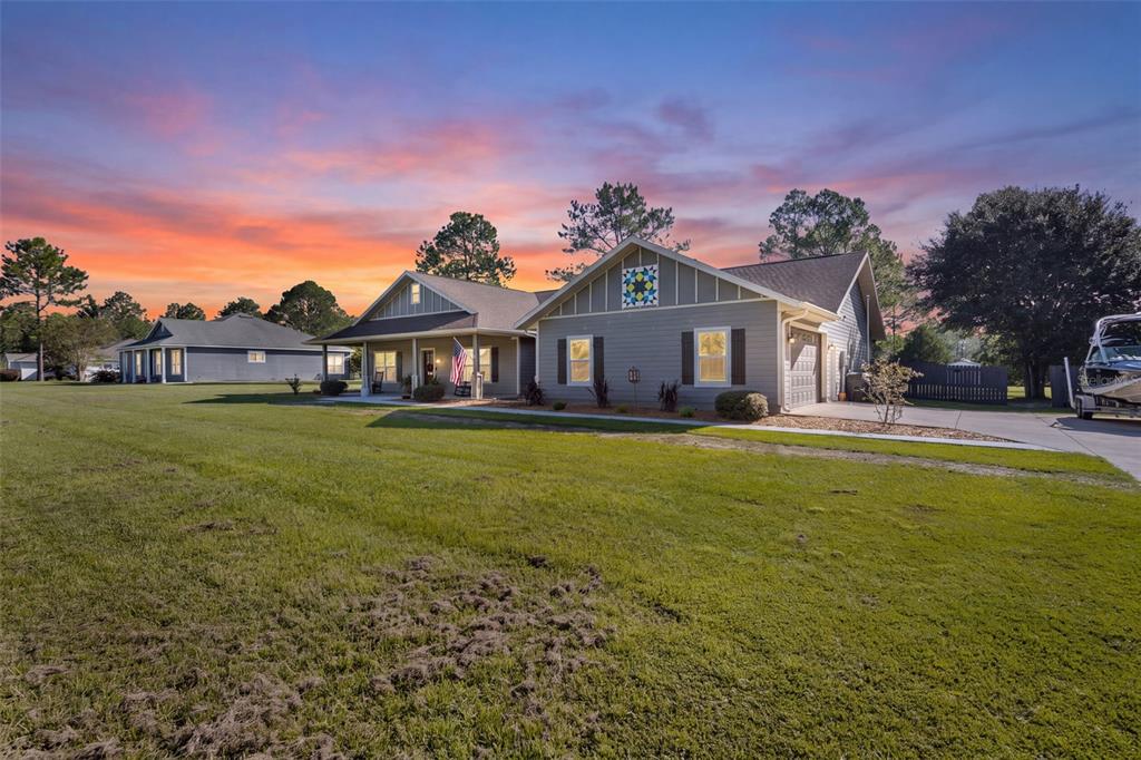A single-story gray house with a front porch, a concrete driveway, and a large lawn — 11311 NW 74TH COURT, CHIEFLAND, FL