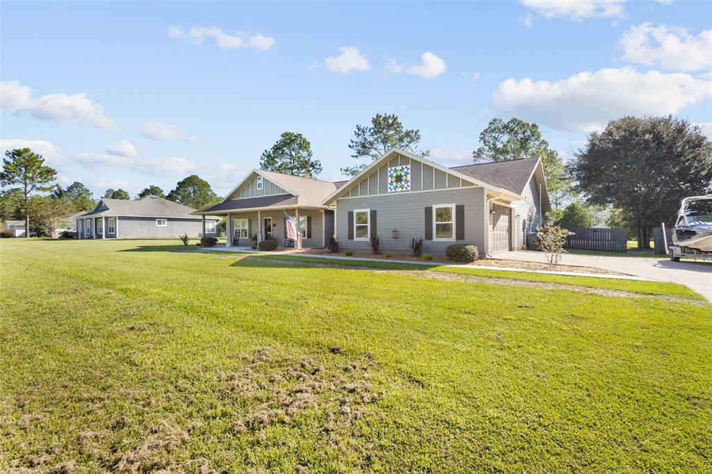 A single-story house with gray siding, a covered front porch, and a quilt-patterned gable accent — 11311 NW 74TH COURT, CHIEFLAND, FL