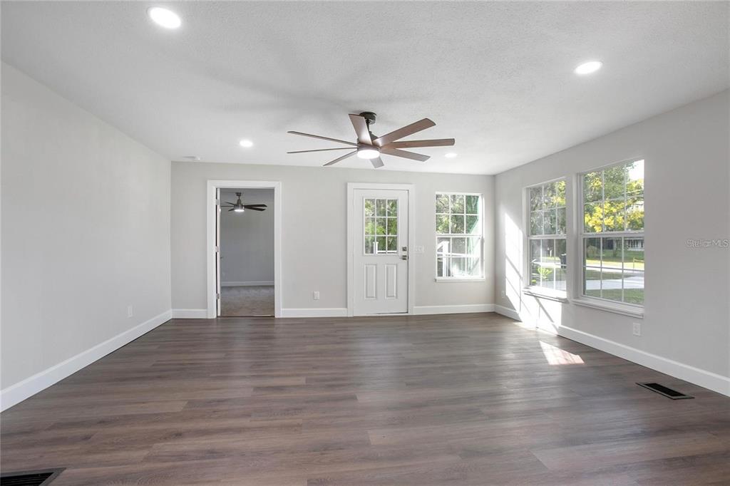 A bright living room features light gray walls, dark wood-look flooring, and a ceiling fan — 1014 TALTON AVE, DELAND, FL