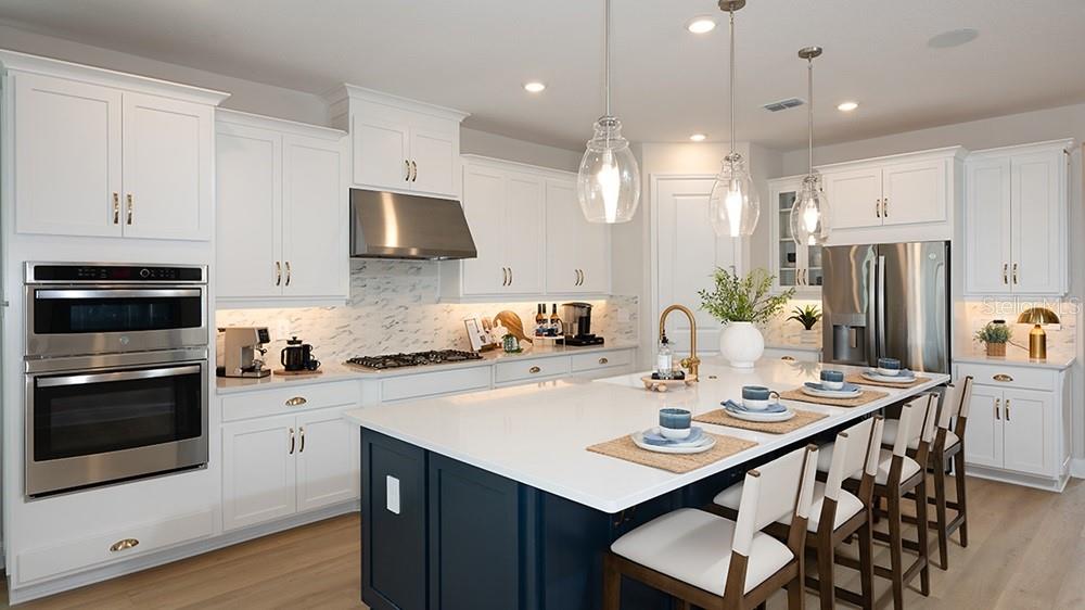 A modern kitchen features white cabinetry, a dark blue island, and stainless steel appliances — 10851 ECLIPSE STREET, SARASOTA, FL