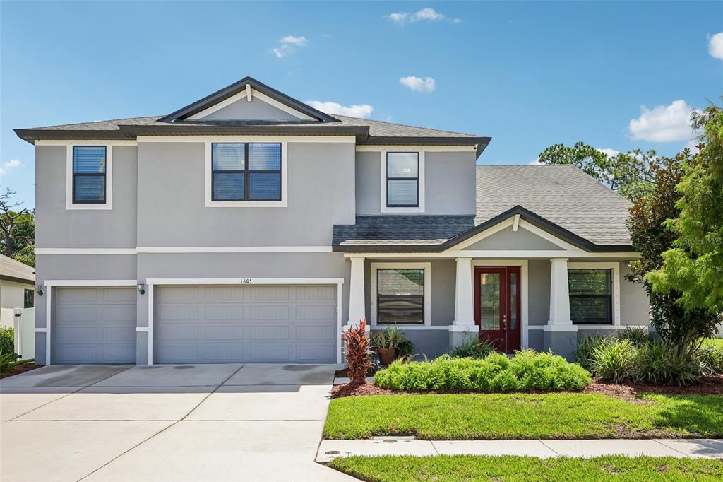 A two-story gray house with a three-car garage, white trim, and a red front door — 1605 ANASTACIA LANE, SUN CITY CENTER, FL