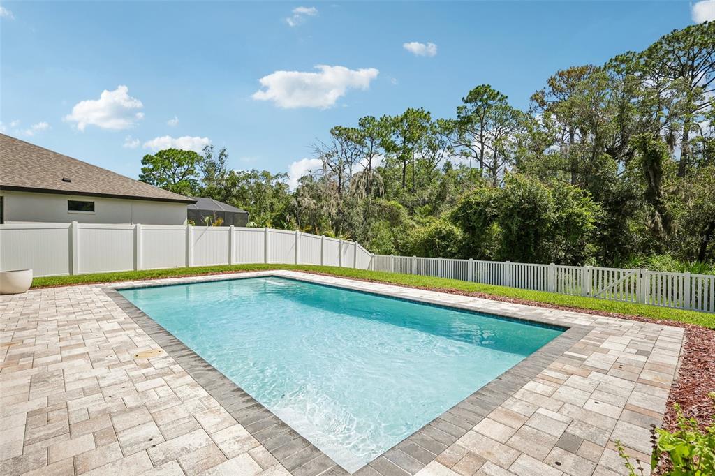 A rectangular swimming pool with a paver deck is enclosed by a white vinyl fence — 1605 ANASTACIA LANE, SUN CITY CENTER, FL