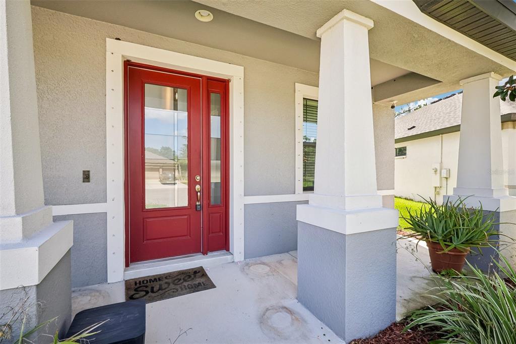 A red front door with a glass panel sits on a covered porch with columns — 1605 ANASTACIA LANE, SUN CITY CENTER, FL