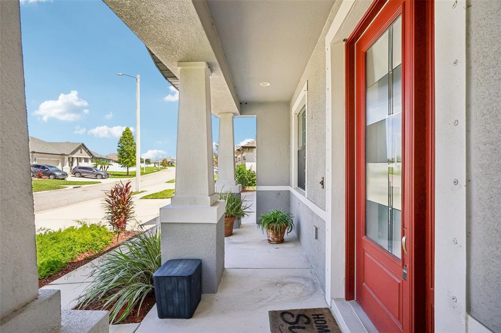 A covered front porch features a red door, concrete flooring, and two white support columns — 1605 ANASTACIA LANE, SUN CITY CENTER, FL
