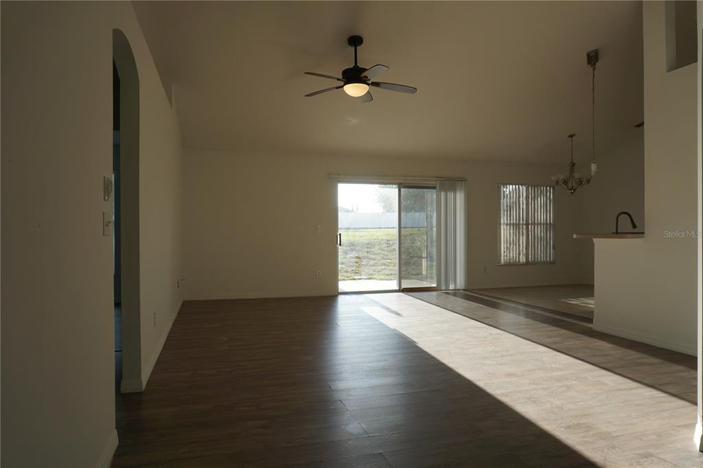 An open-concept living area features wood-look flooring, a ceiling fan, and sliding glass patio doors — 10500 LAKE HASSON CIRCLE, CLERMONT, FL