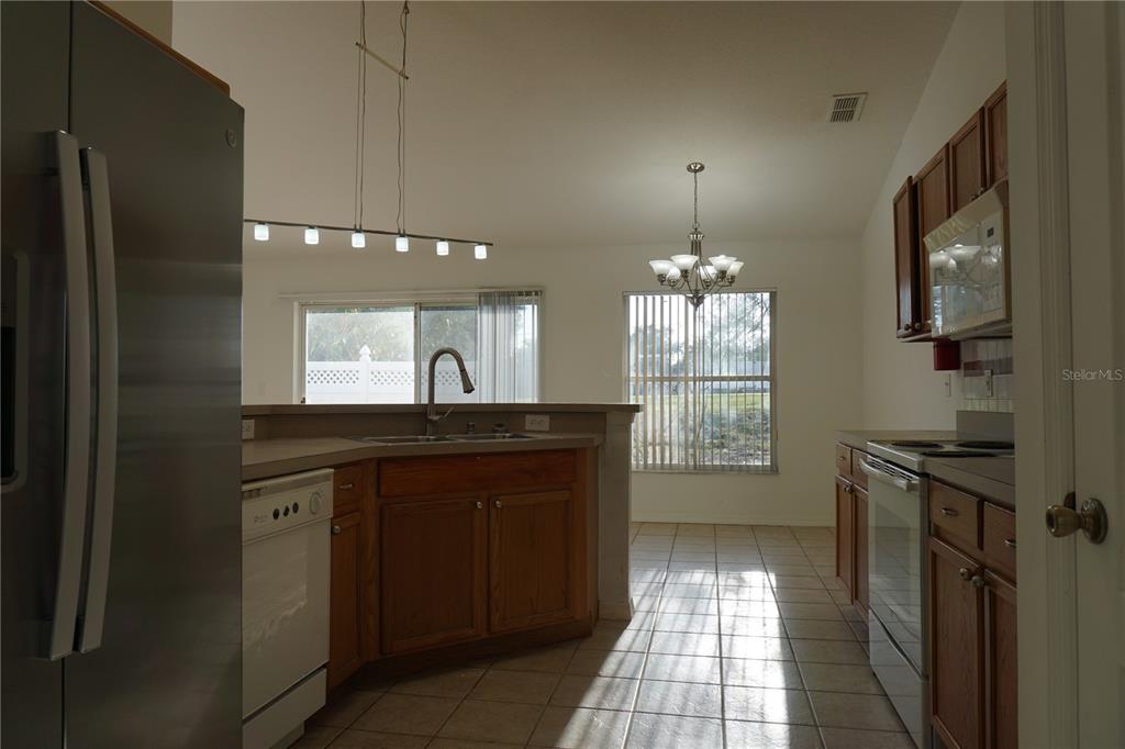A kitchen with wood cabinets, tile floors, and a breakfast bar overlooking a dining area — 10500 LAKE HASSON CIRCLE, CLERMONT, FL