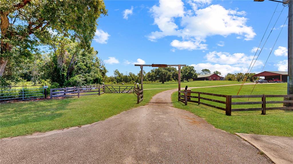 A paved driveway leads through a wooden gate toward a rural property with farm buildings — 12150 SKYVIEW LANE UNIT 0, CLERMONT, FL