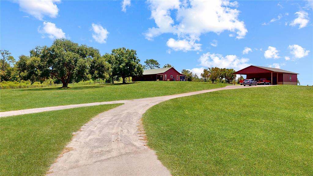 A red house and a detached carport sit on a large, grassy lot with trees — 12150 SKYVIEW LANE UNIT 0, CLERMONT, FL